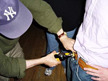 D.A. Powell demonstrating how to open a beer on a young man's belt buckle. Belt buckle: Cheston Knapp. Beer: Newcastle Brown Ale. Photographer: unknown.